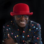 Man wearing a bold red hat with a Pac-Man patterned blazer, exuding confidence.